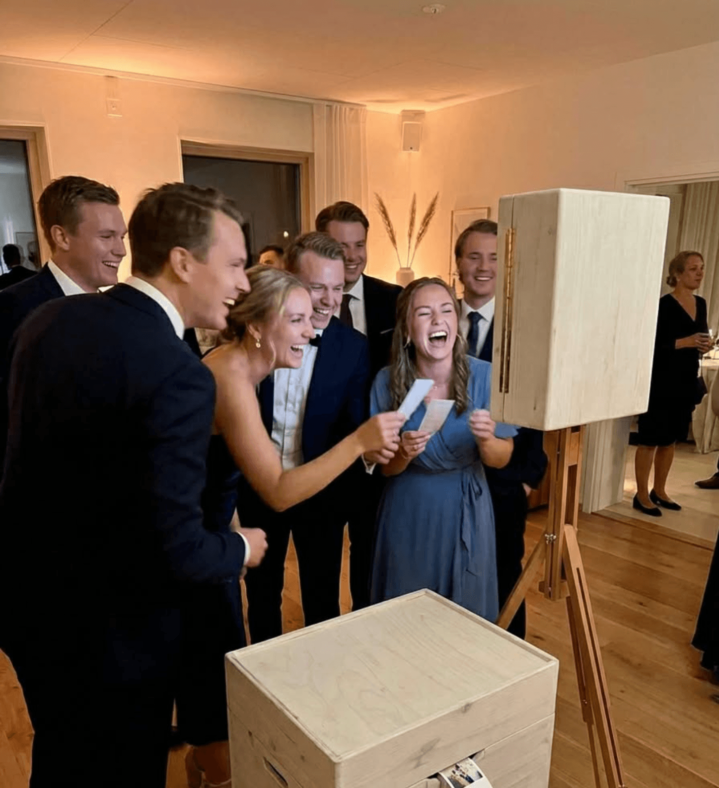 Skrattande bröllopsgäster håller upp en nyutskriven fotoremsa från Maboothens fotobås